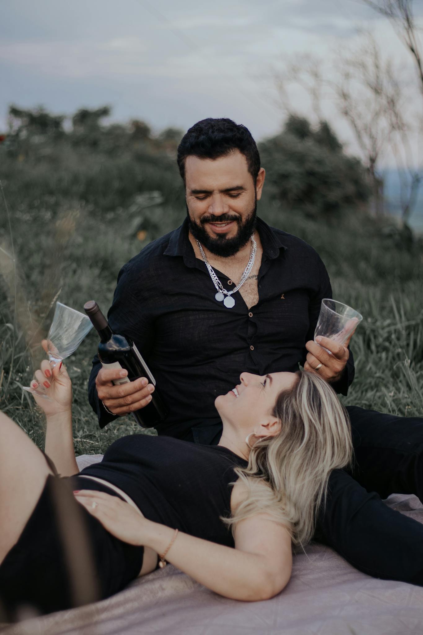 A couple enjoying a romantic picnic with wine in a scenic meadow during summer.