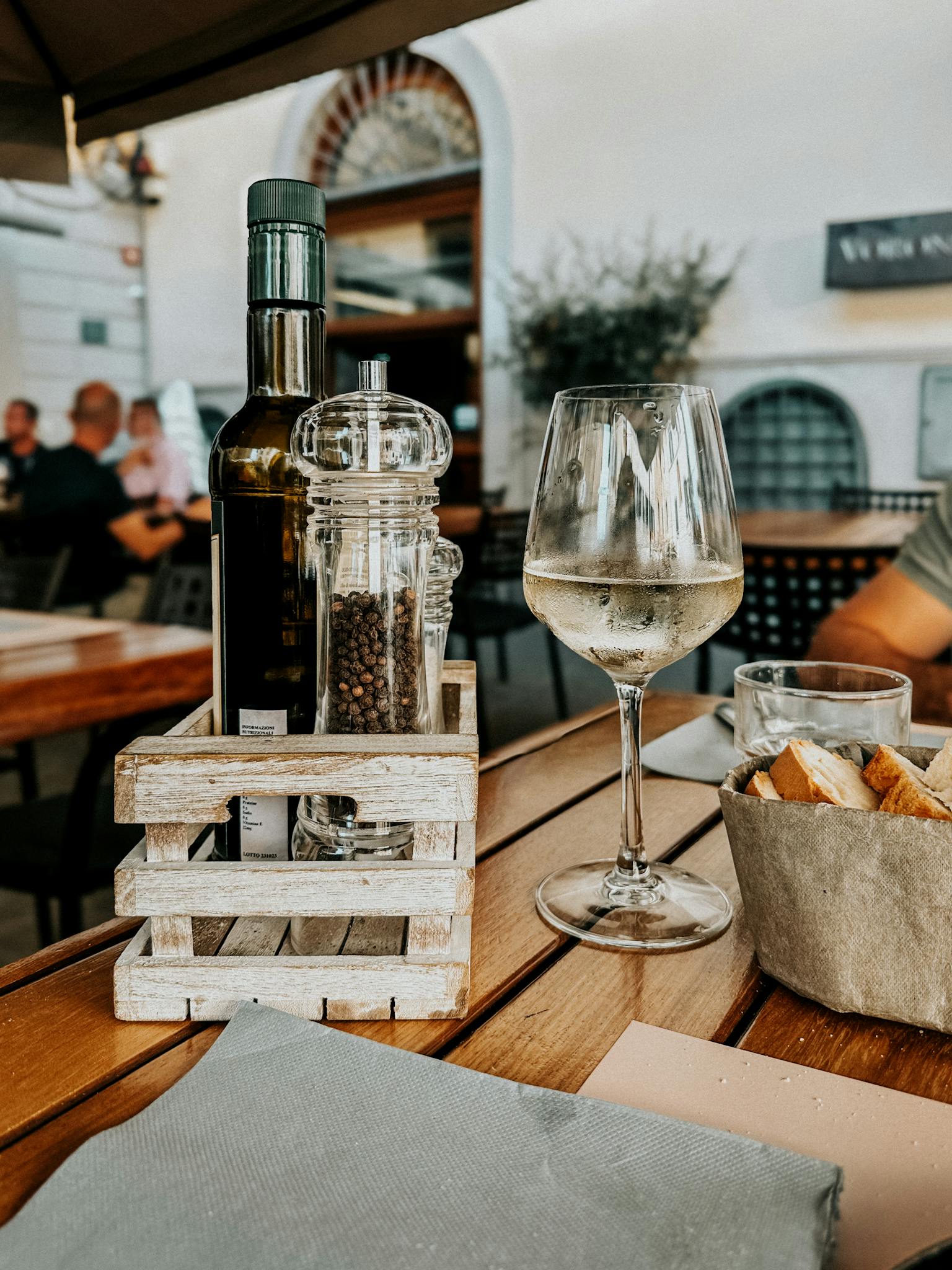 A serene outdoor dining scene in Tuscany featuring a wineglass, spices, and bread on a wooden table.