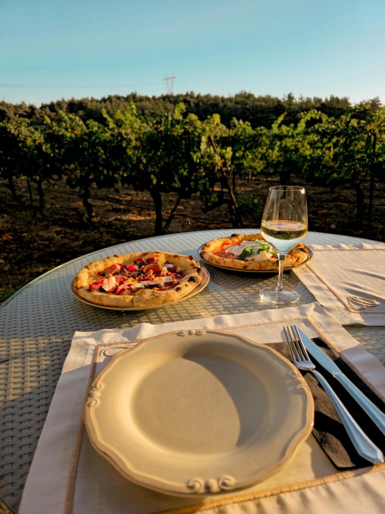 Scenic vineyard view with pizzas and white wine on a table, perfect for outdoor dining ambiance.